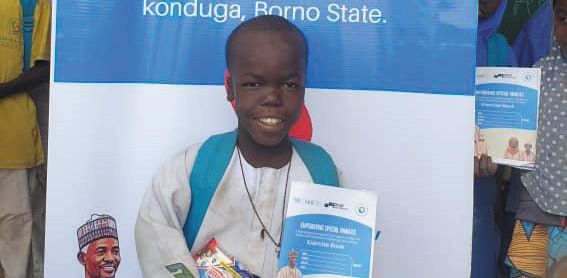 A smiling student holds an education booklet at an event in Konduga, Borno State