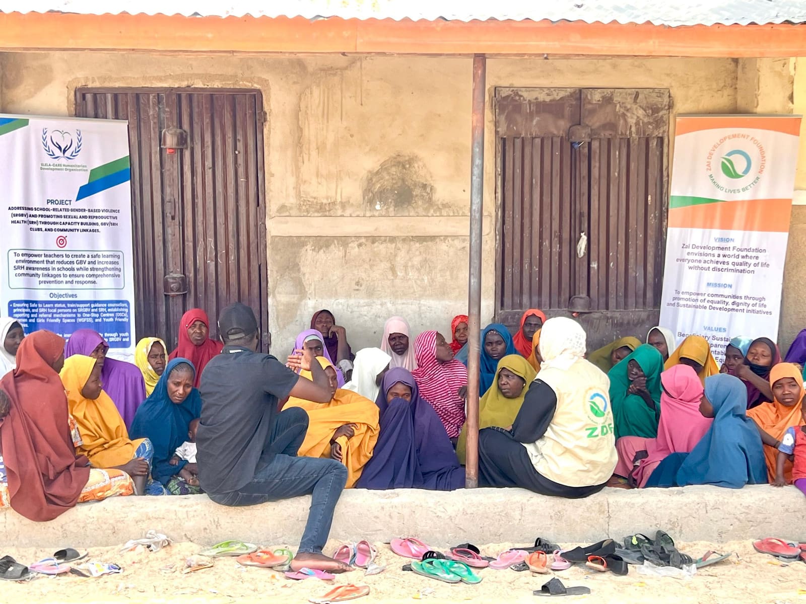 Girls and women seated together outdoors in front of ZAIDF banners