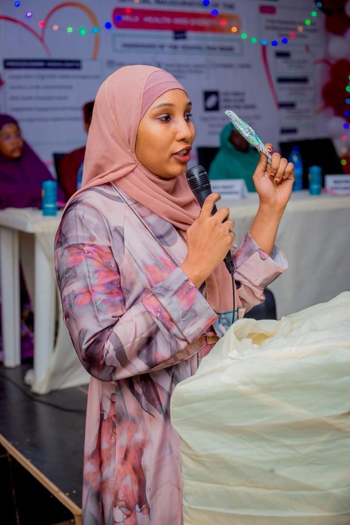 A facilitator speaks into a microphone at a girls' health and dignity event