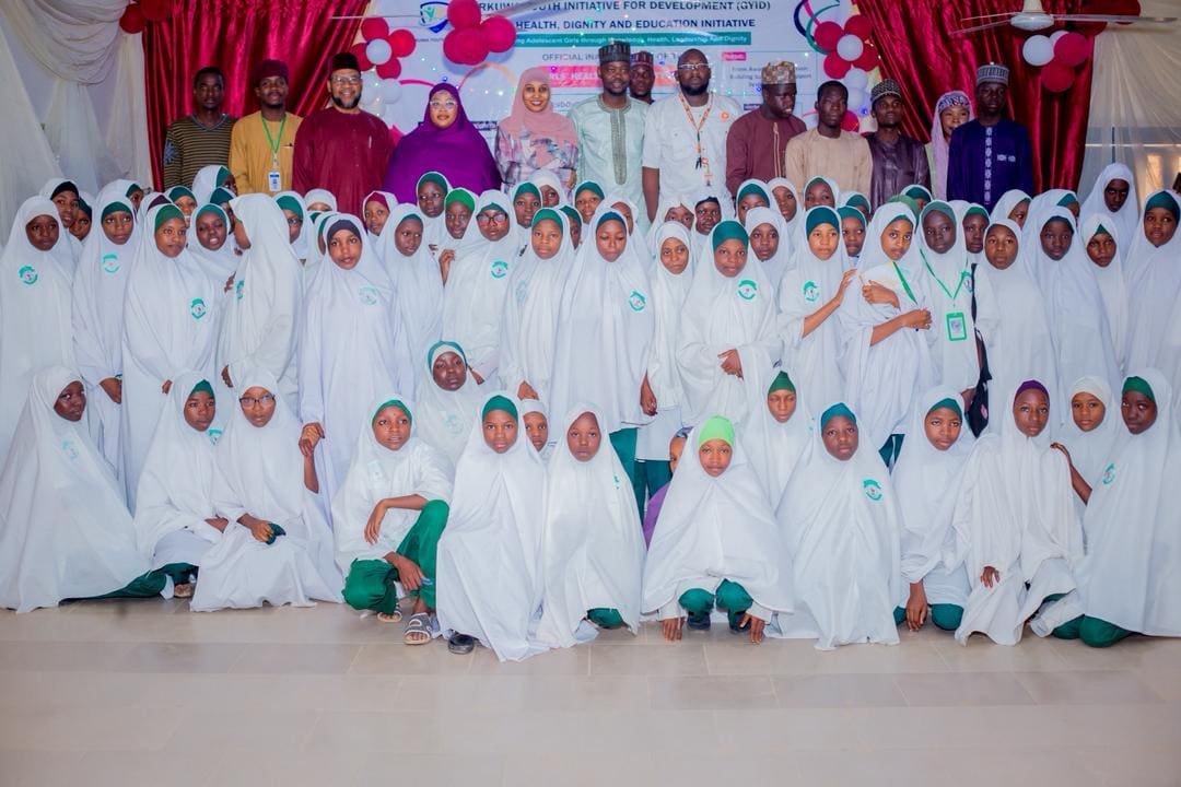 A large group of girls in white headscarves pose with ZAIDF facilitators after a girls' health and dignity session in Abuja