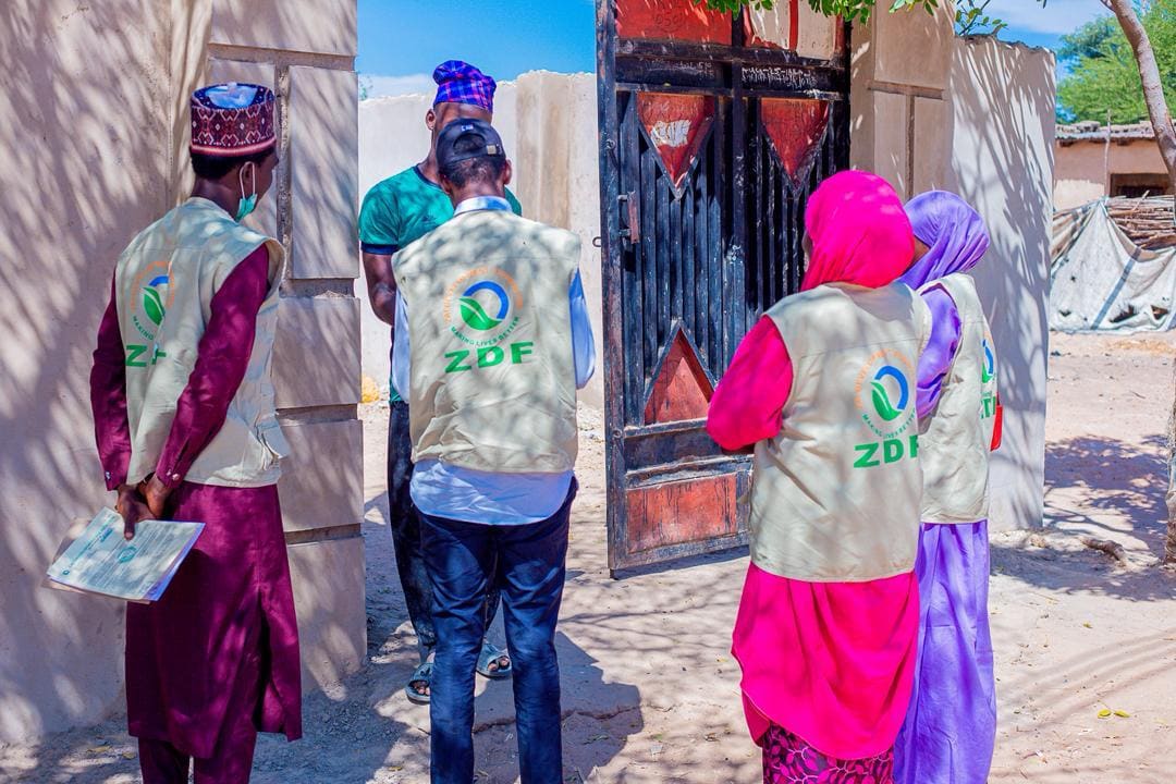 ZAIDF team members in ZDF vests meet women near a compound gate