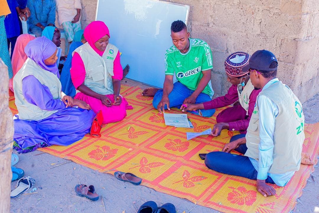 ZAIDF team members and women seated on a mat for a small group discussion