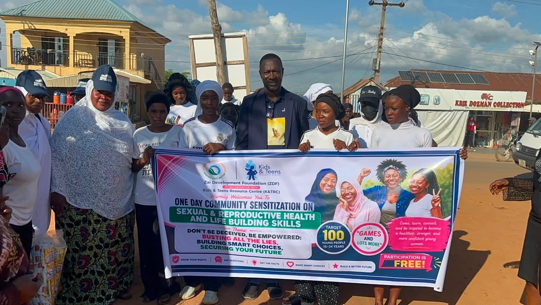 Participants and community members pose behind the banner at a ZAIDF menstrual hygiene session in Abuja